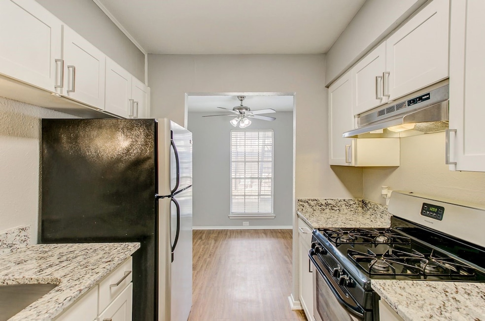 Kitchen with appliances with stainless steel finishes, white cabinetry, light wood finished floors, under cabinet range hood, and ceiling fan