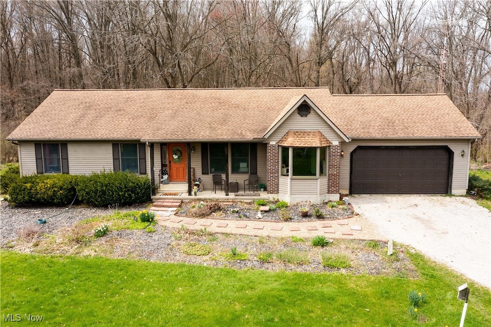 Single story home with a garage, a porch, gravel driveway, and a front lawn