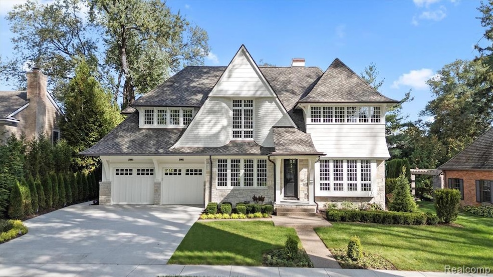 Shingle-style home with stone siding, a front lawn, concrete driveway, and roof with shingles