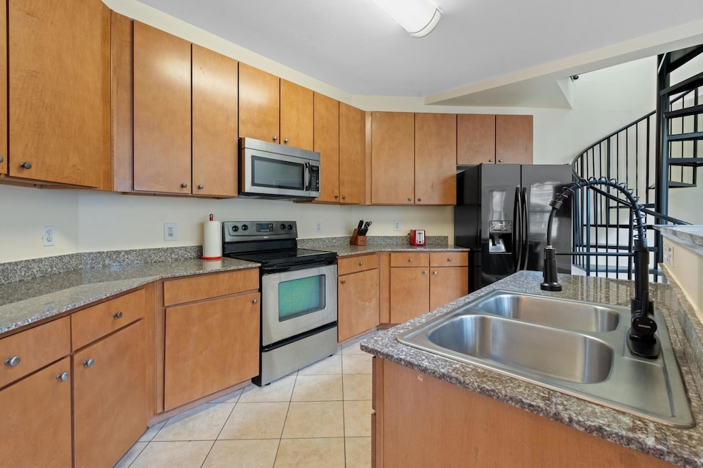 Kitchen with appliances with stainless steel finishes, light tile patterned floors, brown cabinetry, and dark countertops