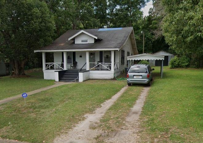 Bungalow-style home featuring dirt driveway, covered porch, a carport, and a front lawn