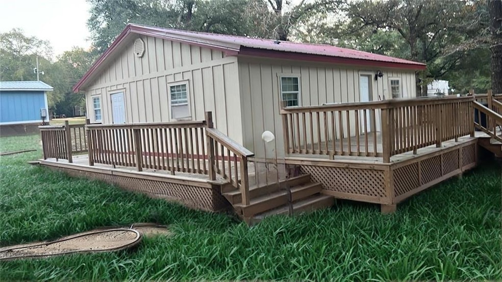Back of house with a wooden deck, board and batten siding, a metal roof, and a lawn