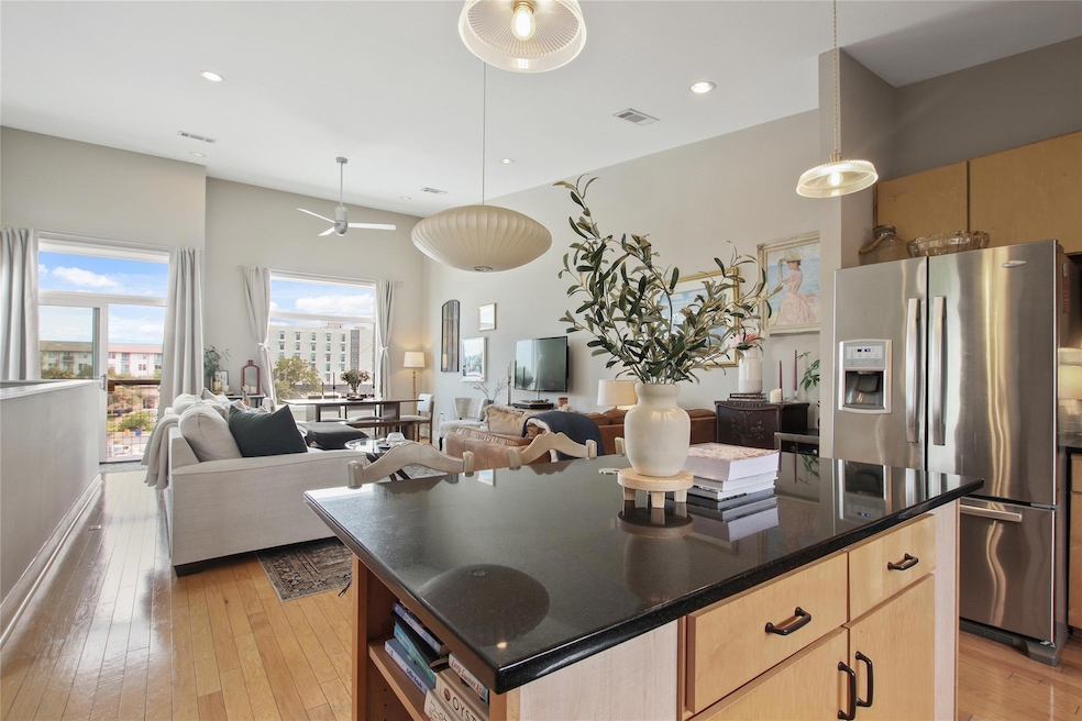 Kitchen with light brown cabinets, decorative light fixtures, stainless steel fridge with ice dispenser, light wood finished floors, and a kitchen island