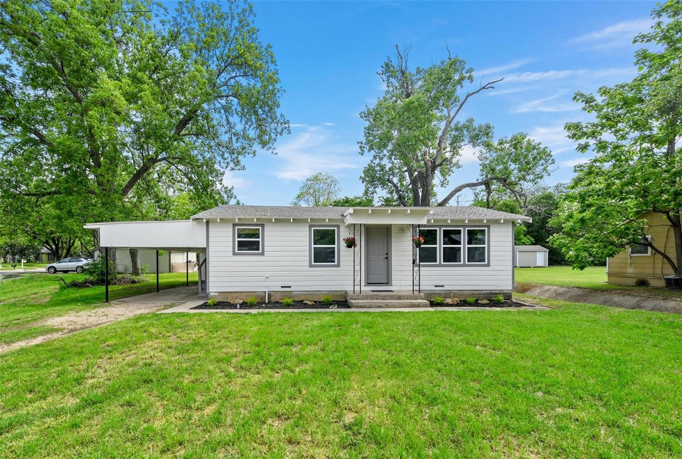 View of front of home featuring a carport, an outdoor structure, and a front lawn