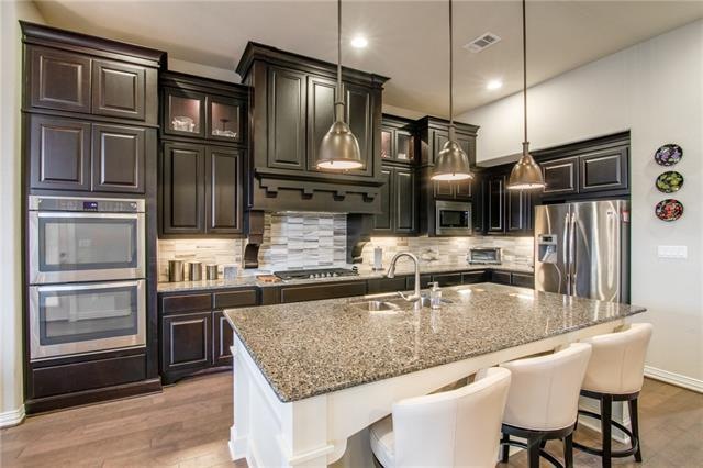Island kitchen features granite counters, tall cabinets (some with glass fronts), a breakfast bar, tile backsplash, pull-out faucet, hardwood flooring, recessed lights, pendant lights over the island, a walk-in pantry, and a butlers pantry.  Stainles