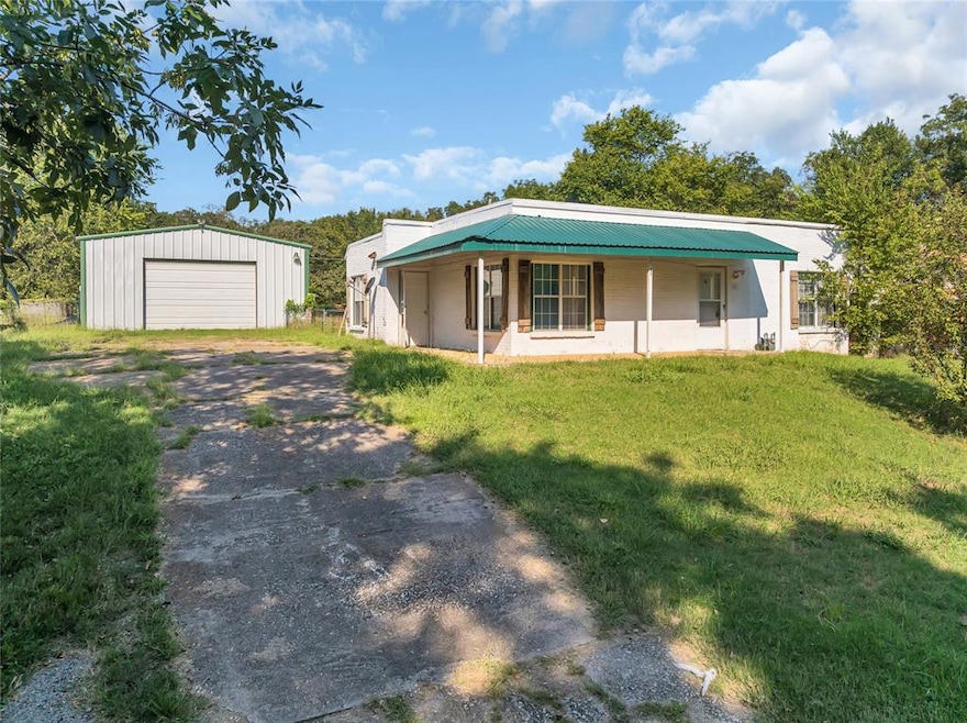 View of front of house with concrete driveway, a detached garage, an outbuilding, a metal roof, and a porch