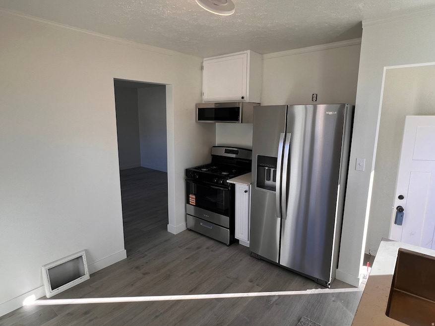 Kitchen featuring white cabinetry, stainless steel appliances, a textured ceiling, dark wood-style flooring, and light countertops