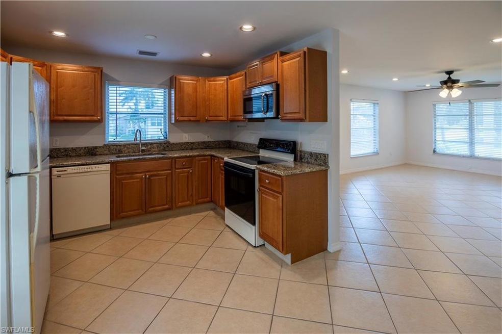 Kitchen featuring white appliances, brown cabinetry, recessed lighting, light tile patterned floors, and open floor plan