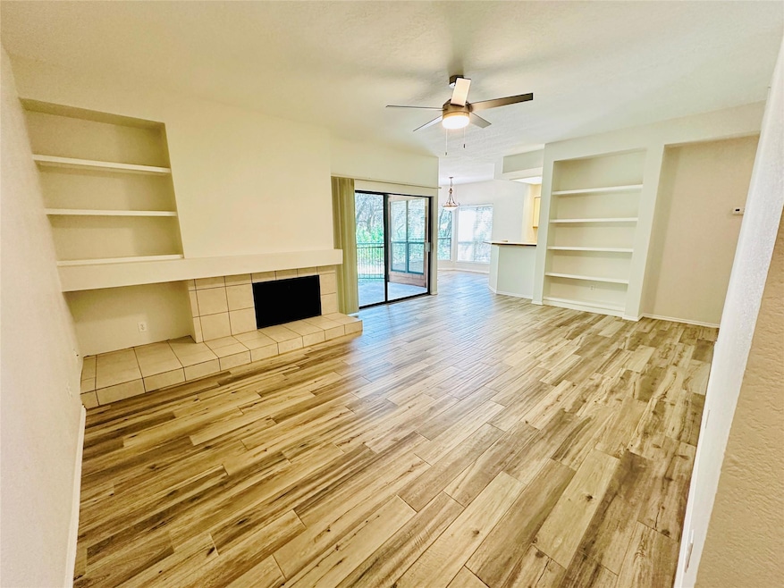 Unfurnished living room with built in shelves, a tile fireplace, ceiling fan, light wood-style floors, and a chandelier