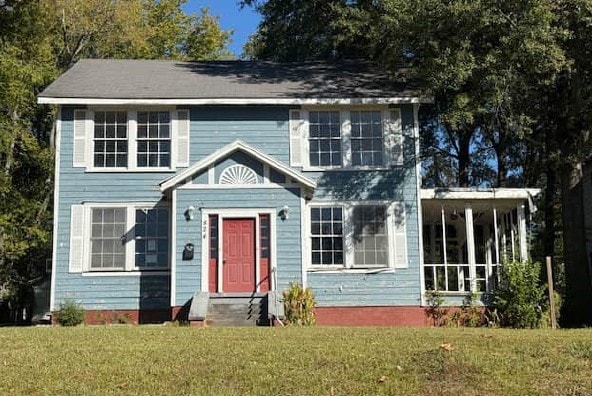 Colonial-style house featuring a front yard, a sunroom, and entry steps