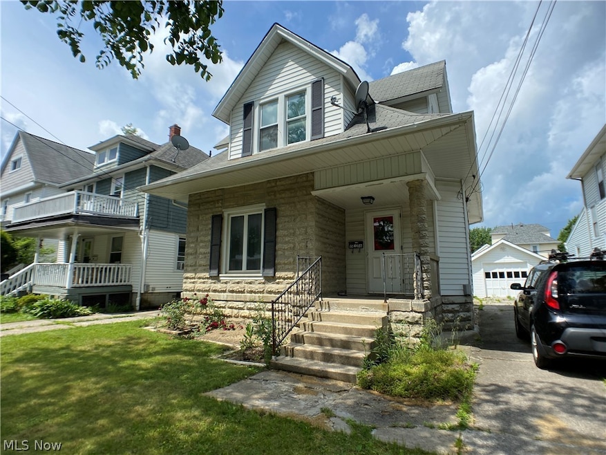 View of front of property featuring a porch, an outdoor structure, a garage, and a front yard
