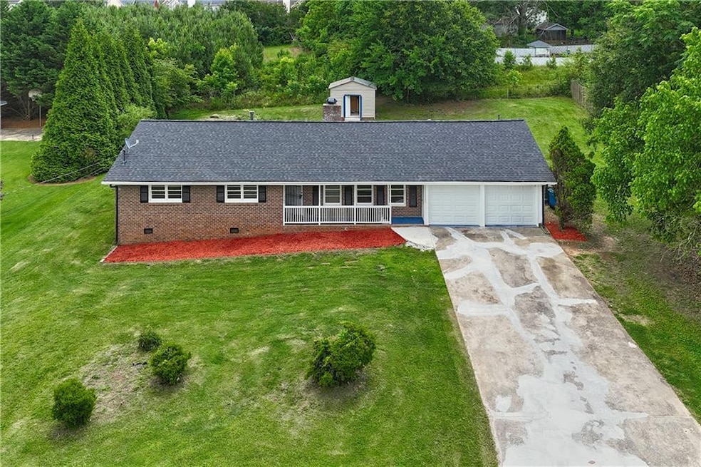 View of front of property featuring covered porch, brick siding, a garage, concrete driveway, and crawl space