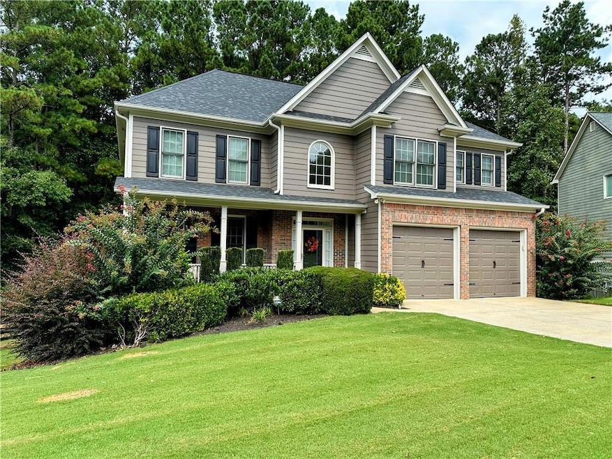 View of front of house featuring a front yard, driveway, a garage, covered porch, and brick siding