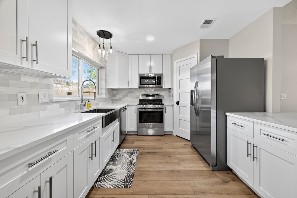 The heart of the home, this gourmet kitchen features pristine white cabinetry, stainless steel appliances, a farmhouse sink, and contemporary backsplash.