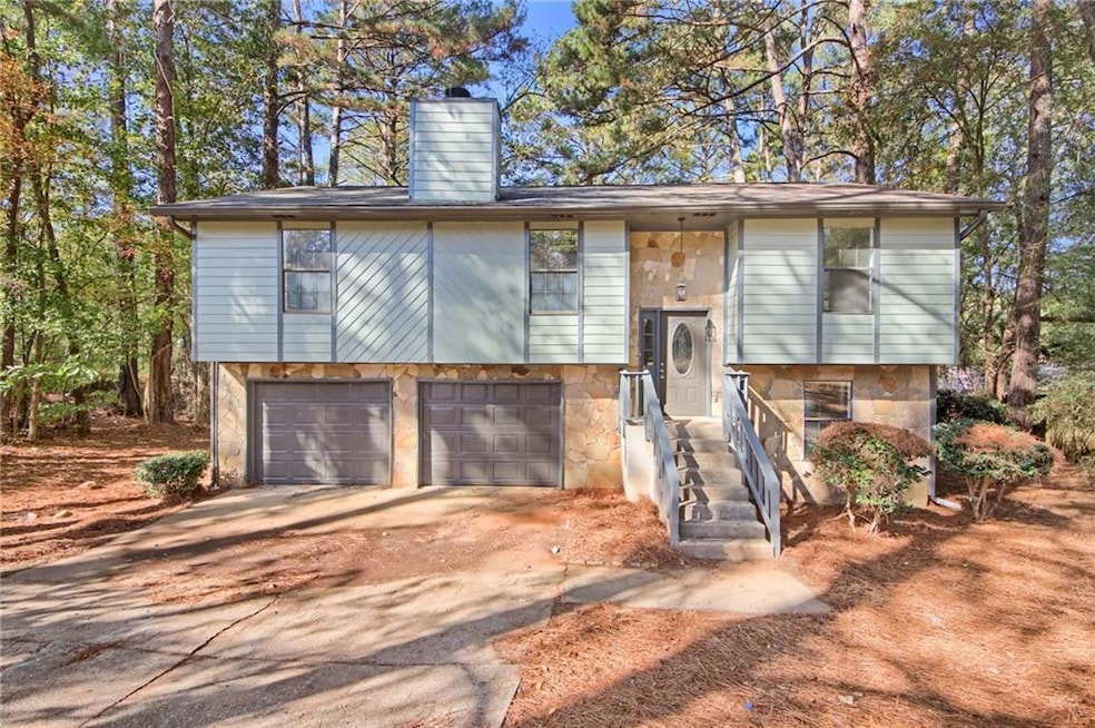Split foyer home featuring a chimney, concrete driveway, stone siding, and a garage