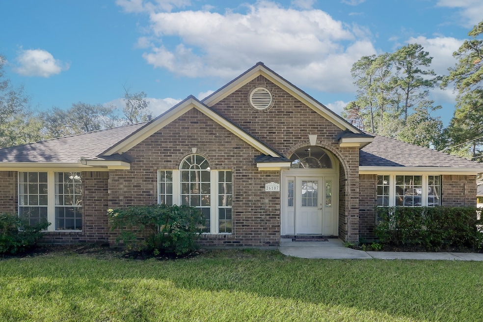 This charming single-story brick home features large windows and a welcoming entrance. It is surrounded by a well-maintained lawn and framed by mature trees, providing a serene and inviting atmosphere.