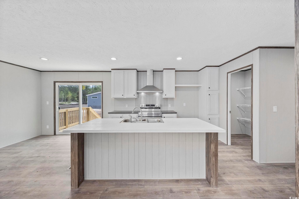 Kitchen with wall chimney exhaust hood, white cabinets, a kitchen island with sink, light wood finished floors, and a textured ceiling