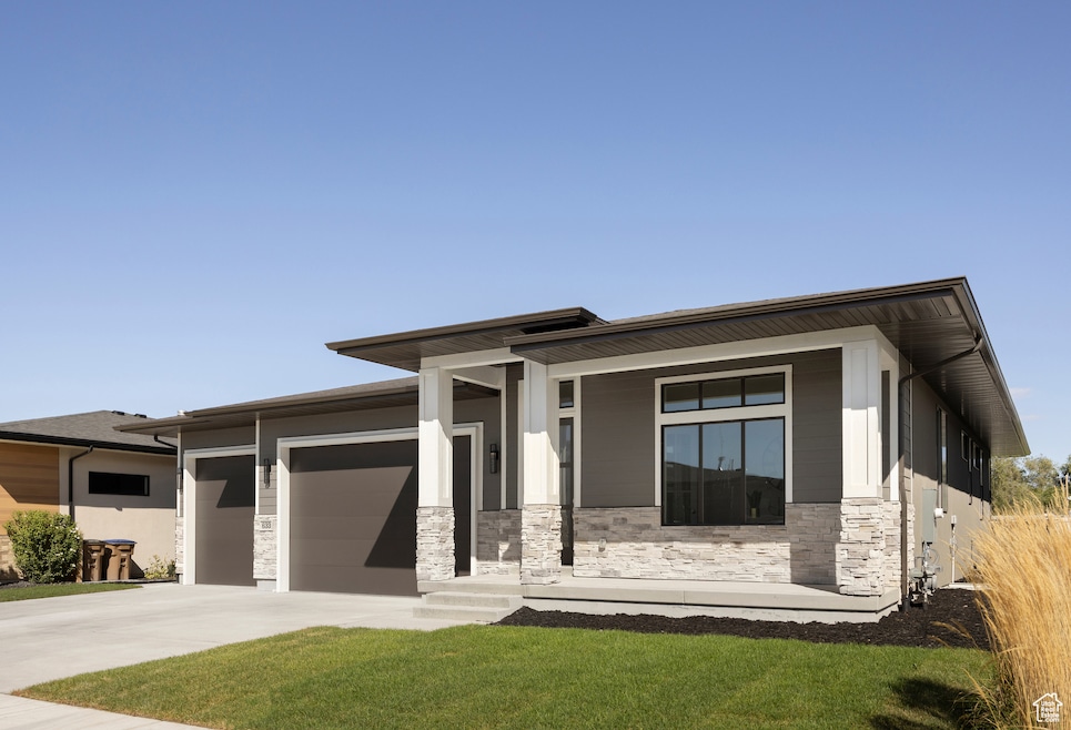 Prairie-style home featuring stone siding, a porch, driveway, an attached garage, and a front lawn