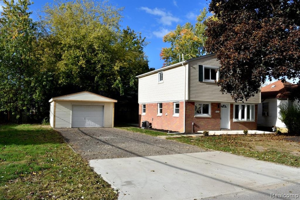 View of front of house featuring brick siding, concrete driveway, an outbuilding, a garage, and a front yard