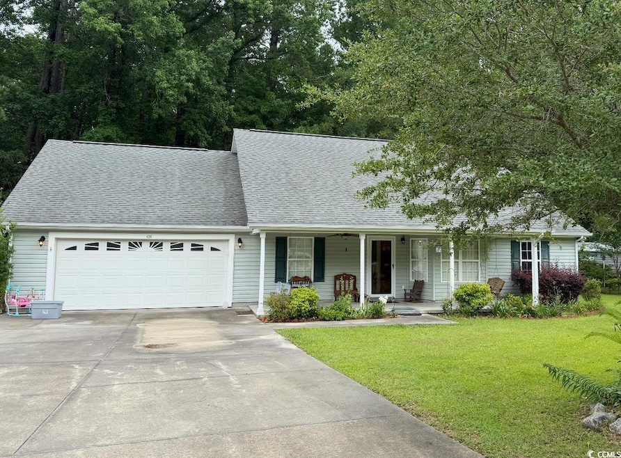 View of front of property with concrete driveway, roof with shingles, an attached garage, covered porch, and a front yard