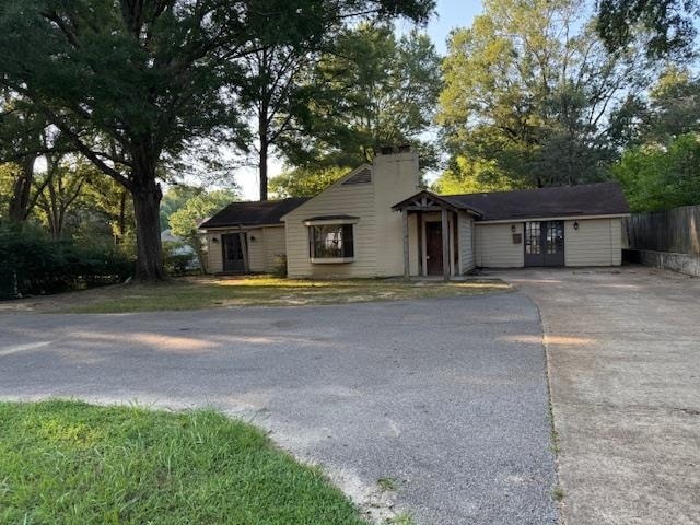 Ranch-style home featuring driveway, french doors, a chimney, and view of scattered trees