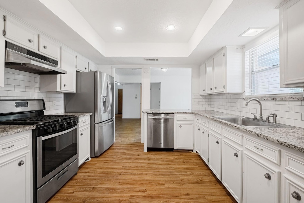 Kitchen with stainless steel appliances, a tray ceiling, decorative backsplash, white cabinets, and light wood-type flooring
