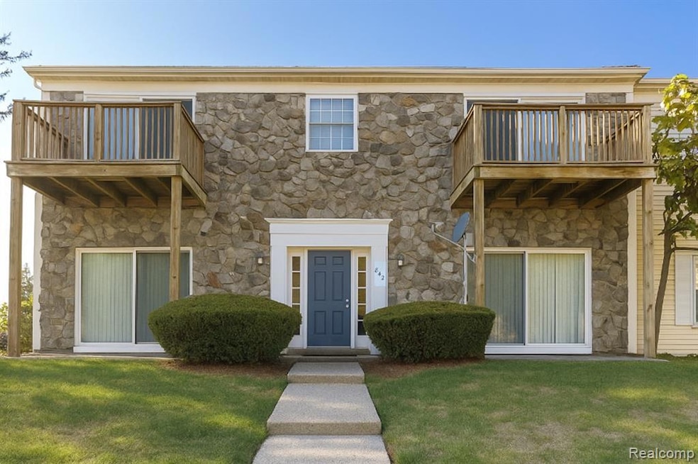 View of front facade featuring stone siding, a balcony, and a front yard