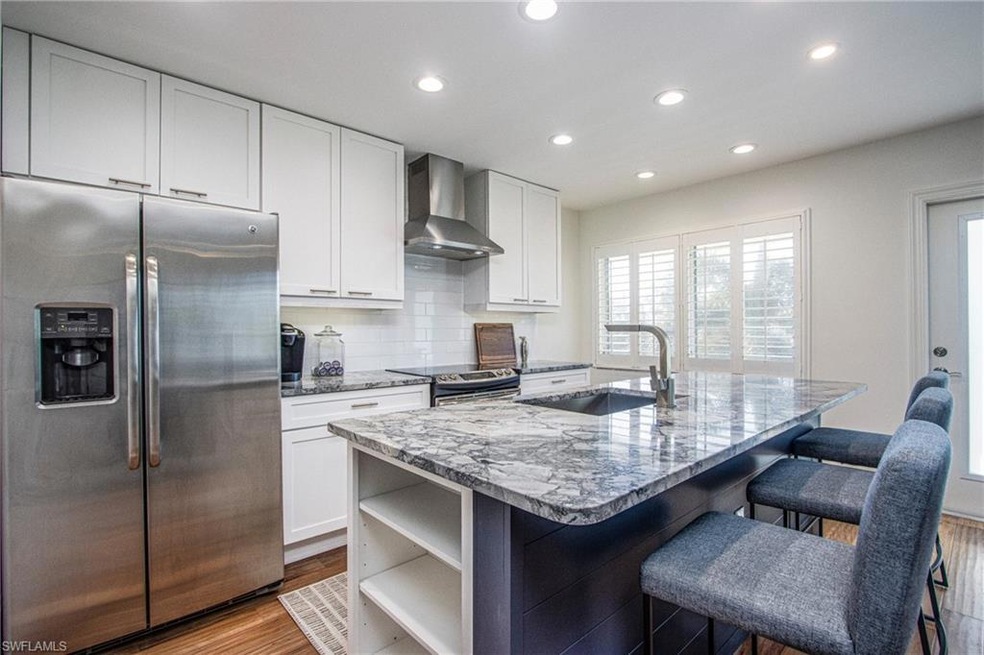 Kitchen featuring appliances with stainless steel finishes, light stone countertops, wall chimney range hood, open shelves, and a sink