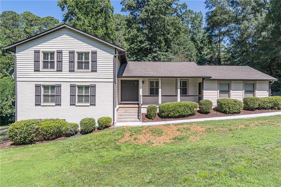 Tri-level home with covered porch, a front lawn, and a shingled roof