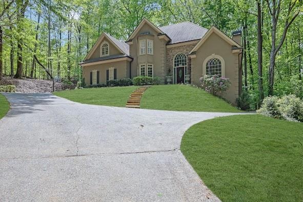 View of front of home featuring a chimney, stucco siding, driveway, stone siding, and a front yard
