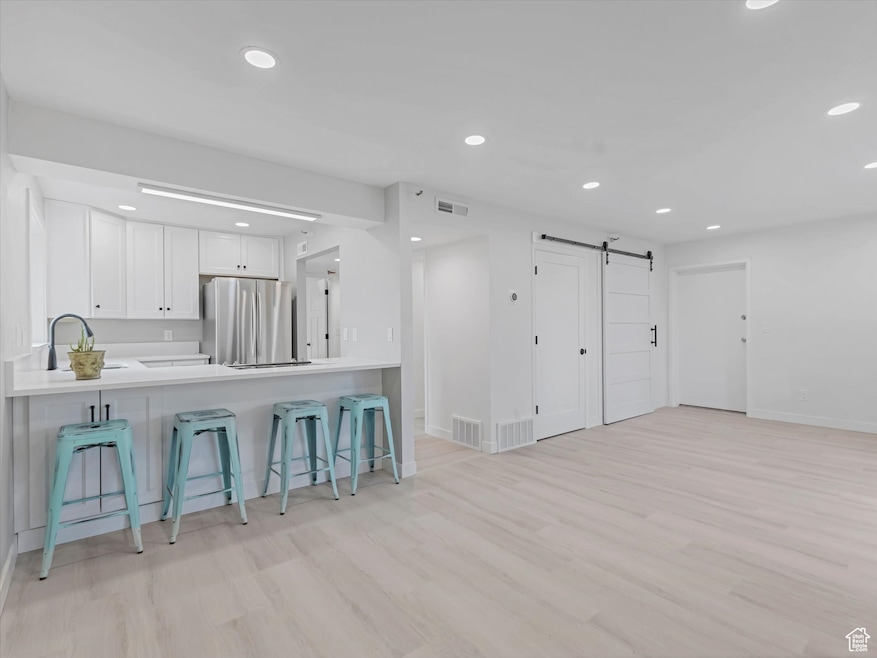 Kitchen featuring a barn door, a kitchen bar, light wood-style flooring, white cabinetry, and recessed lighting