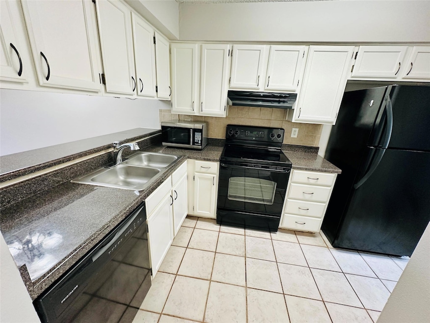 Kitchen with black appliances, white cabinetry, light tile patterned floors, decorative backsplash, and under cabinet range hood