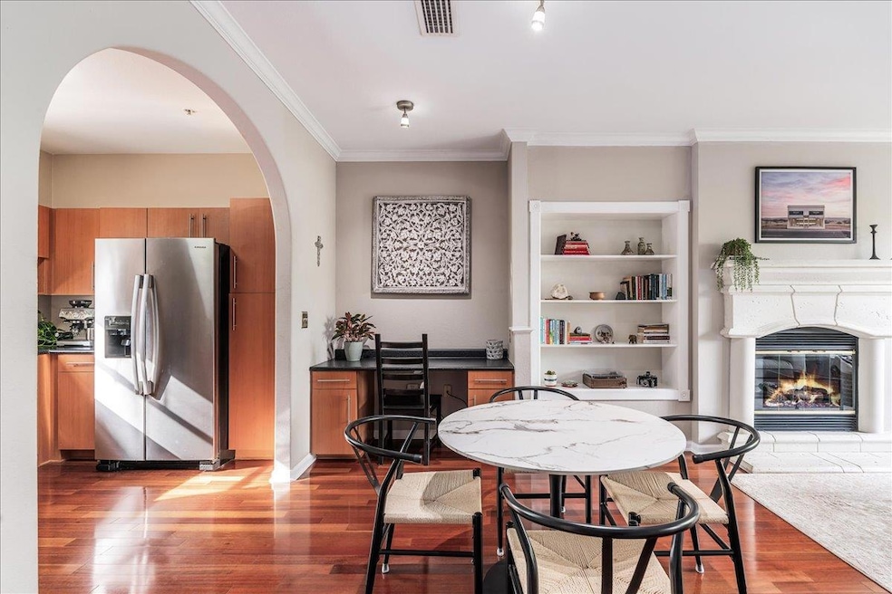 Dining space with ornamental molding, arched walkways, light wood finished floors, a glass covered fireplace, and built in features