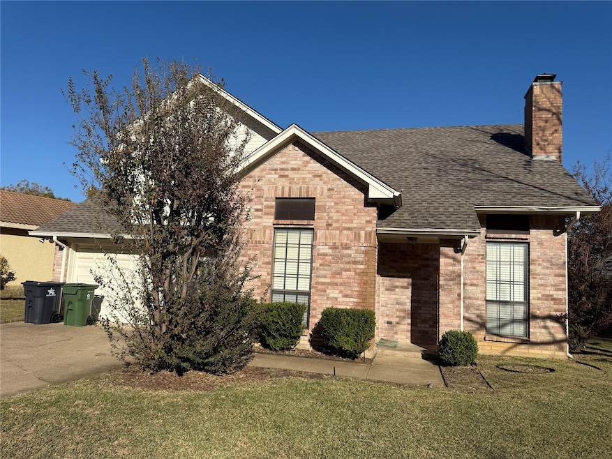 View of front of property featuring a front lawn, a chimney, a shingled roof, brick siding, and driveway