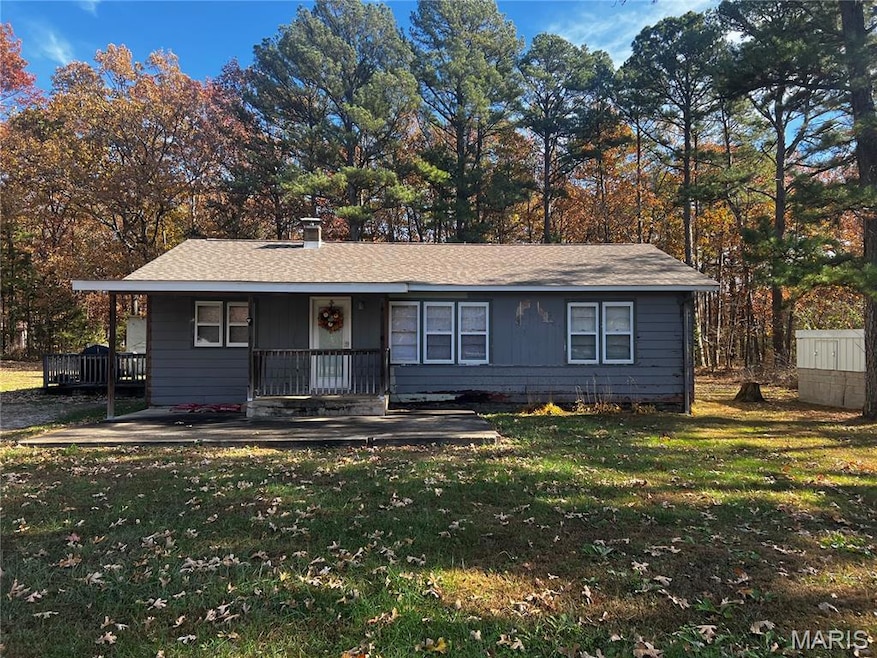 View of front of house featuring covered porch, a shingled roof, view of scattered trees, and a chimney
