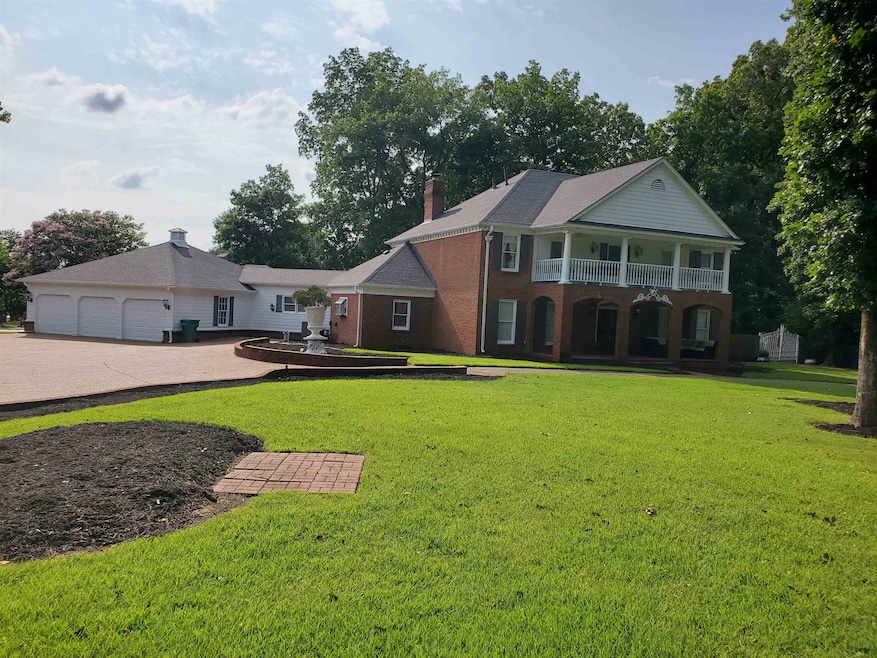 View of front facade featuring a front lawn, a balcony, concrete driveway, a chimney, and brick siding