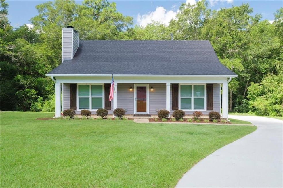View of front facade featuring a chimney, a front lawn, concrete driveway, covered porch, and a shingled roof
