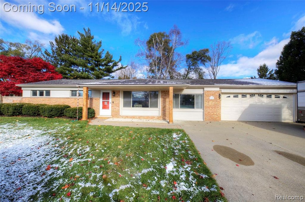 Ranch-style home featuring brick siding, a front lawn, concrete driveway, an attached garage, and covered porch