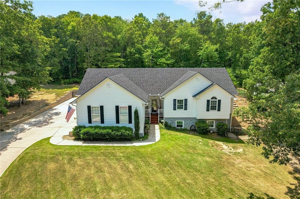 View of front of property featuring a front lawn, driveway, a shingled roof, and a wooded view