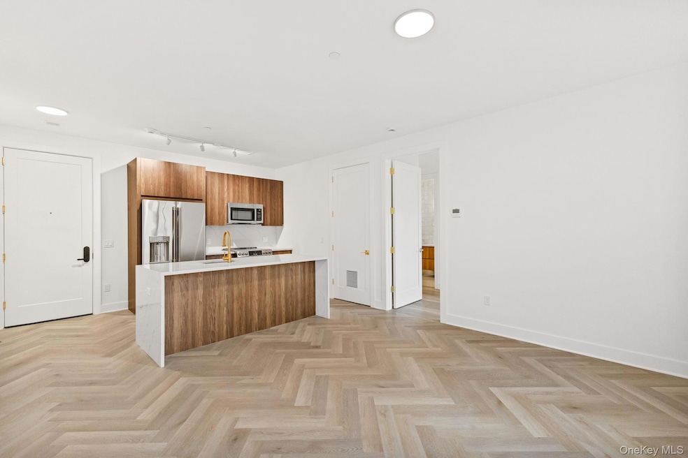 Kitchen featuring brown cabinetry, modern cabinets, light stone countertops, stainless steel appliances, and a center island with sink