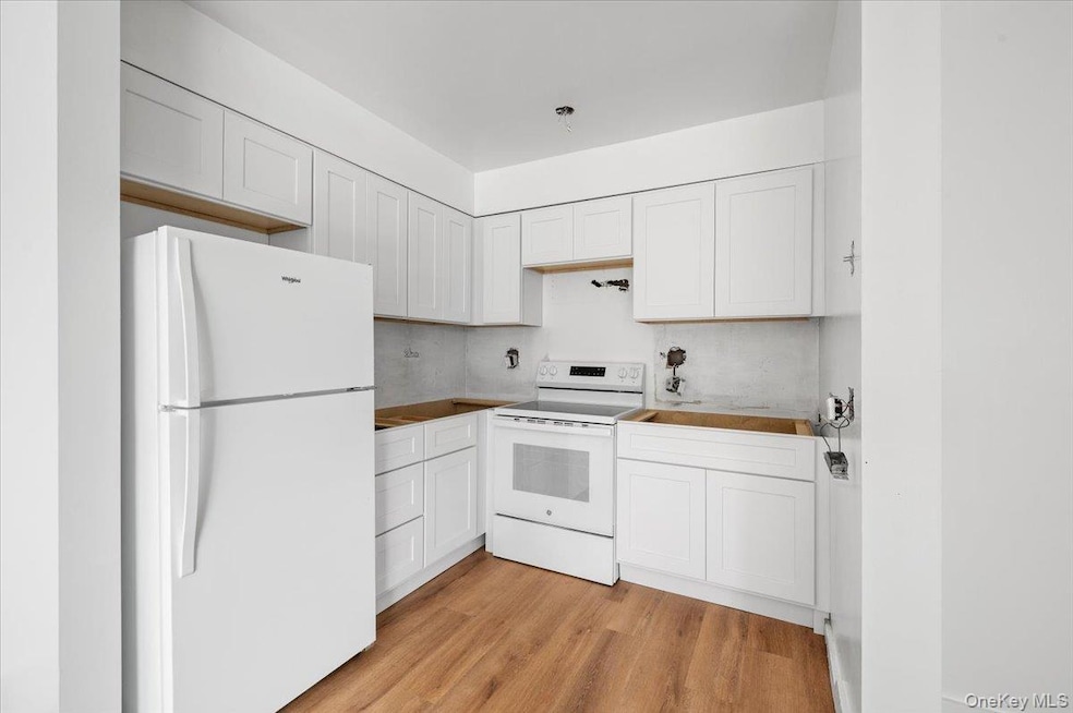Kitchen with white appliances, light wood finished floors, and white cabinetry
