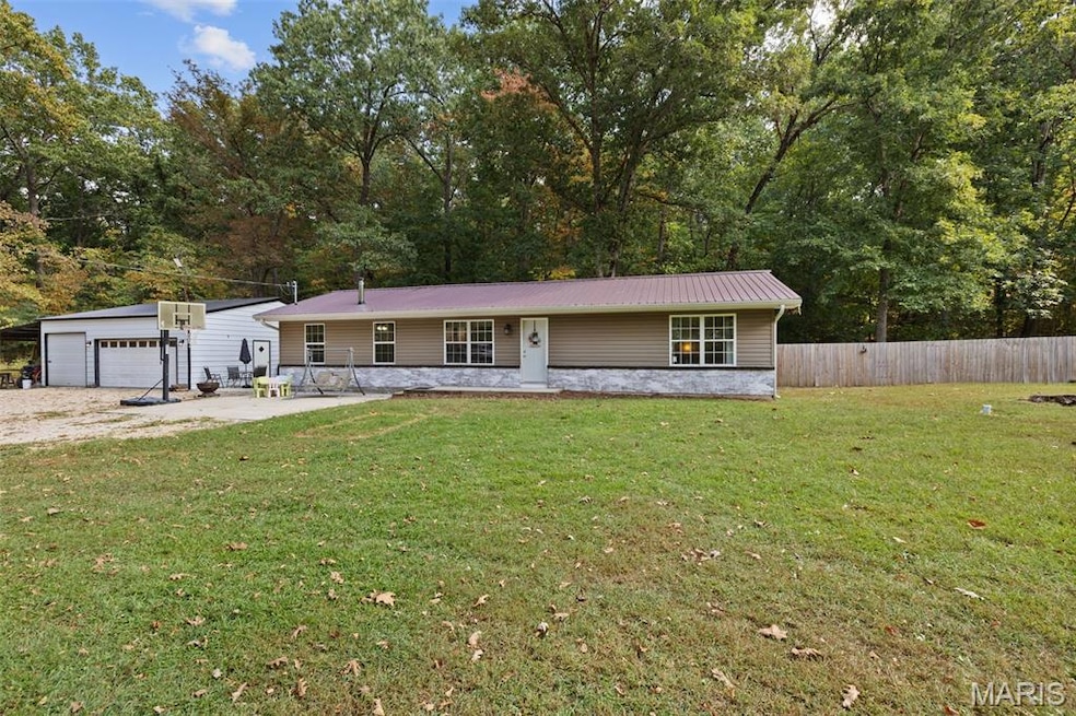 Single story home with a metal roof, view of scattered trees, and a patio