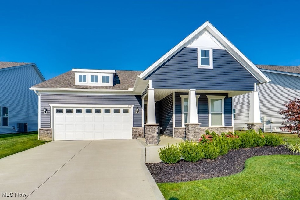 View of front of house with a porch, roof with shingles, an attached garage, driveway, and stone siding
