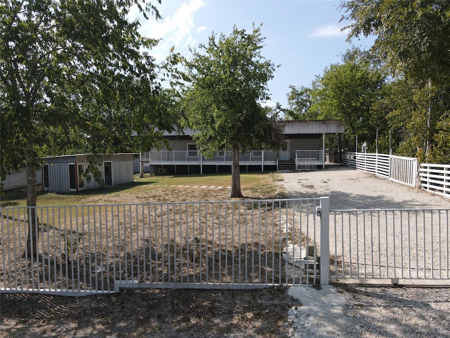 View of front of house with gravel driveway, an outbuilding, and a gate
