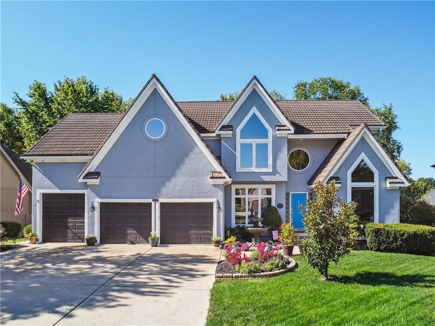 1- View of front featuring driveway, a front yard, stucco siding, metal roof, several windows and lots of beautiful landscaping