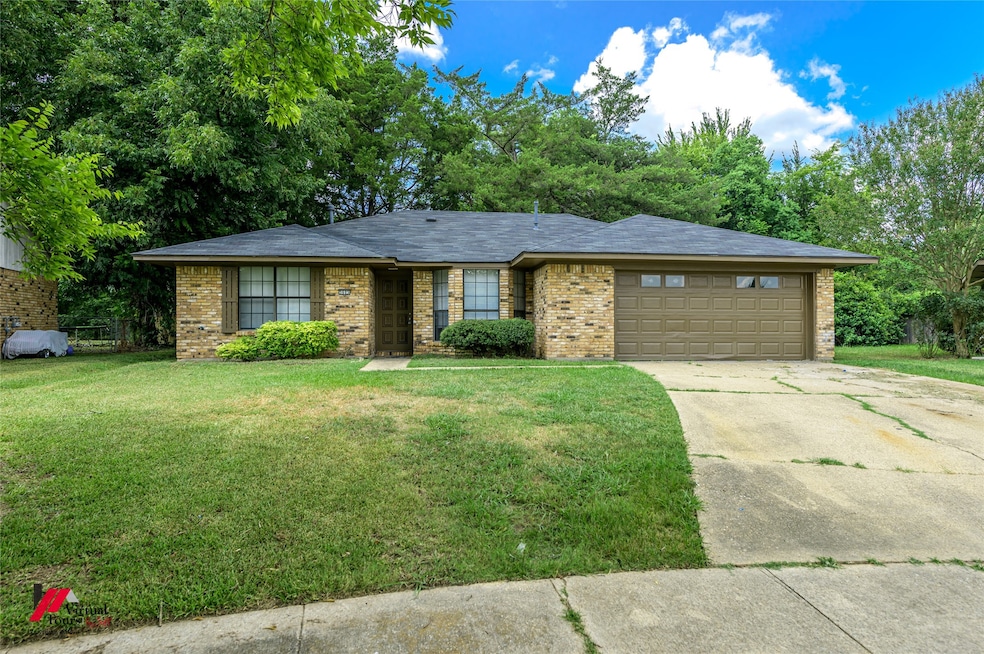 Single story home featuring an attached garage, concrete driveway, brick siding, and a front yard