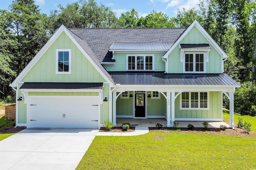 View of front of property with board and batten siding, covered porch, a front lawn, concrete driveway, and a garage
