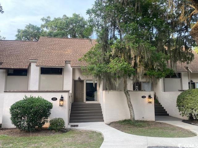 View of front of property with stairs, a shingled roof, and stucco siding