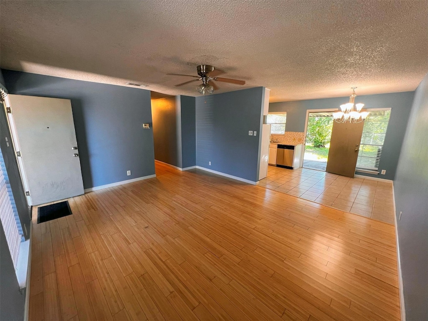 Unfurnished living room featuring a chandelier, a ceiling fan, a textured ceiling, and light wood-style floors