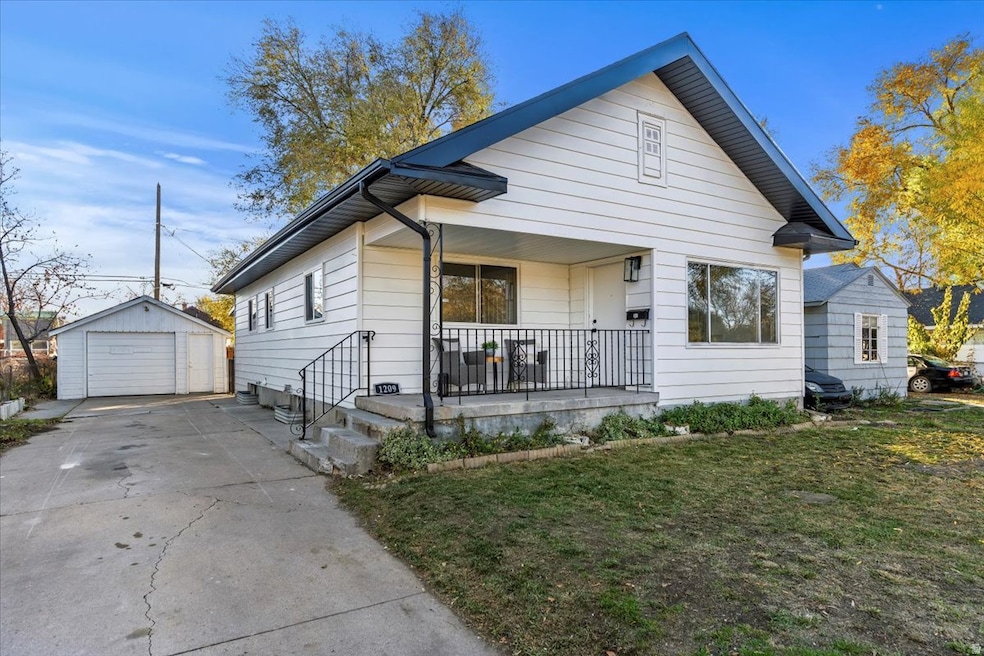 Bungalow-style house with a porch, a detached garage, a front yard, an outbuilding, and concrete driveway